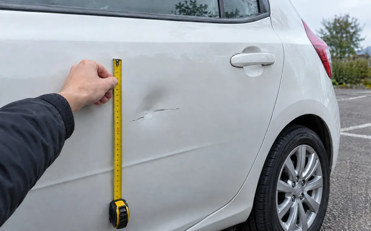 Delle an einer Autotür wird mit dem Maßband vermessen